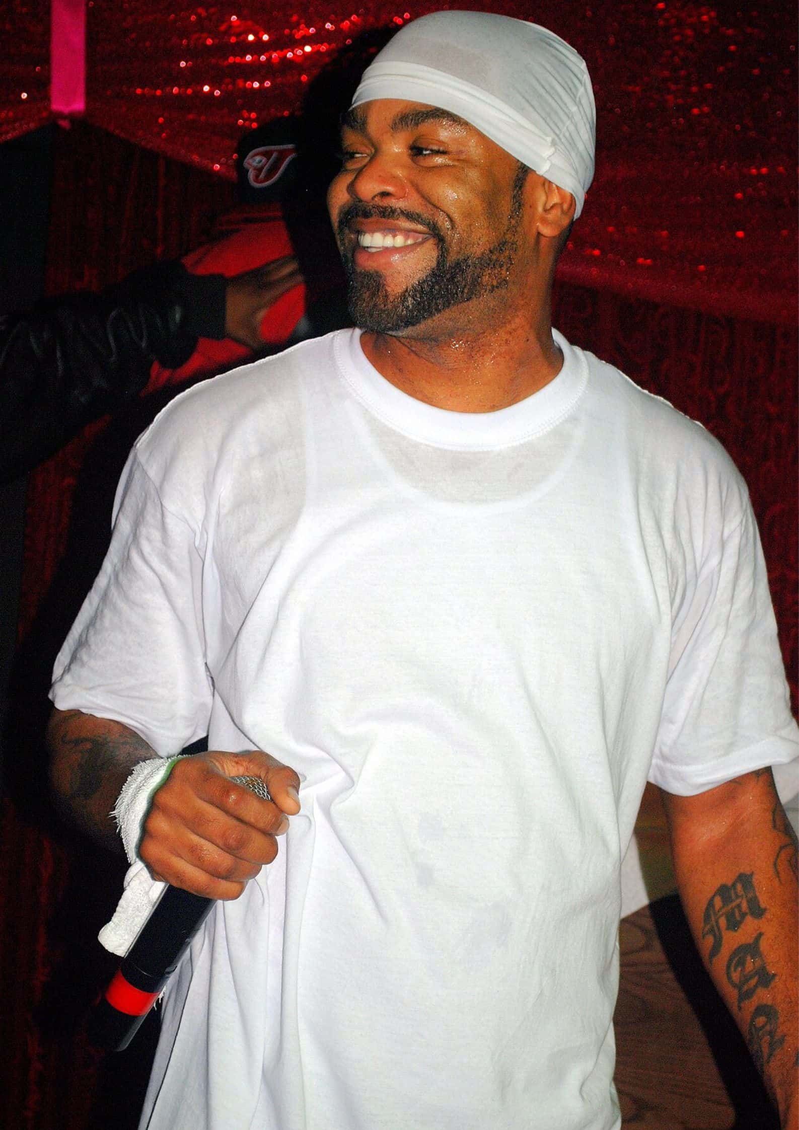 Method Man (Clifford Smith) from Wu-Tang Clan wearing a red striped polo shirt and red cap, performing on stage.