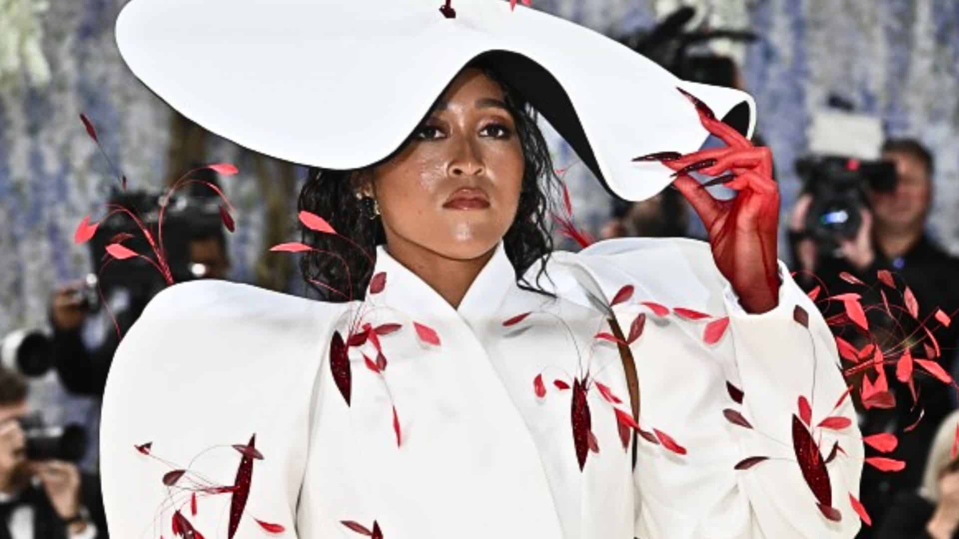 Naomi Osaka wearing an avant-garde white couture look with oversized sculptural hat and red floral accents