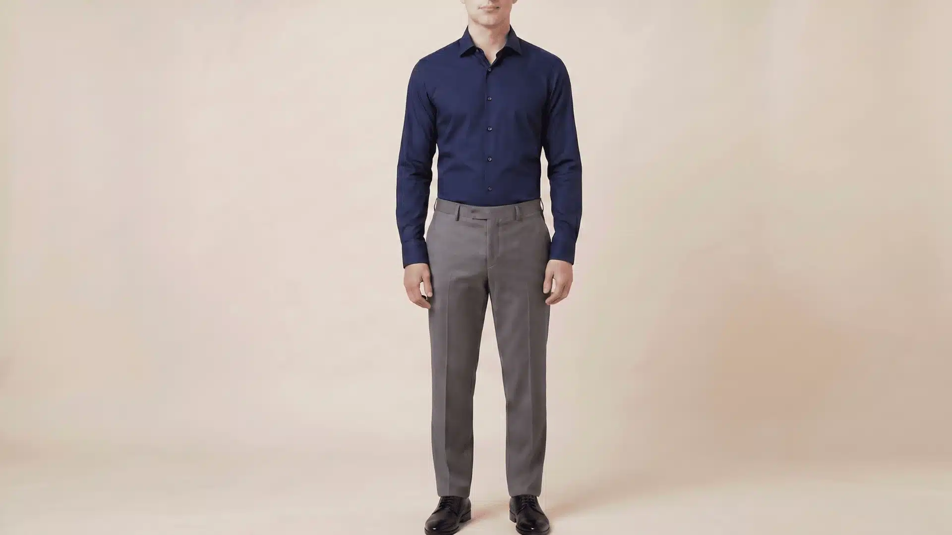 Man wearing a navy blue, long-sleeve shirt with charcoal grey pants and black shoes, standing in a neutral background.