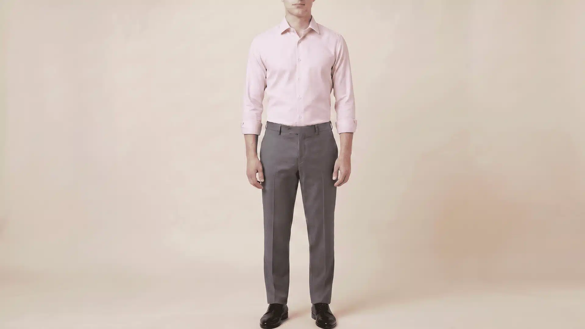 Man wearing a pink long-sleeve shirt with charcoal grey pants and black shoes, standing in a neutral background.