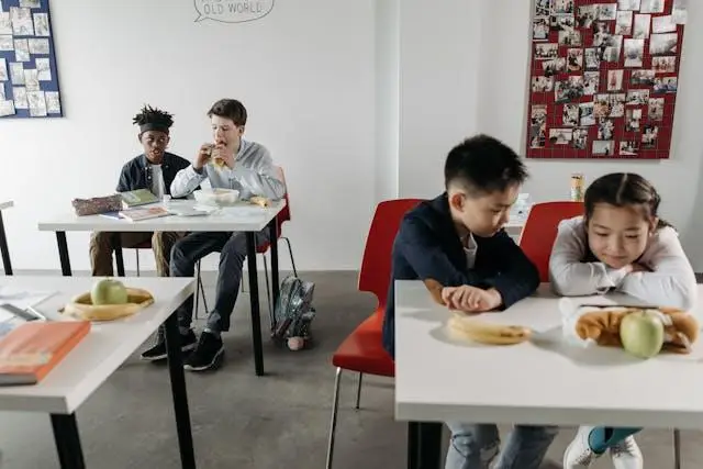 Children eating lunch in a classroom with books and apples on tables