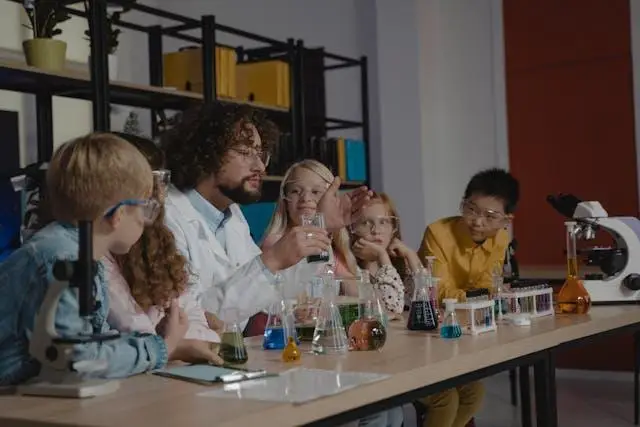 Teacher explaining science experiment to children at lab table with colorful beakers and flasks