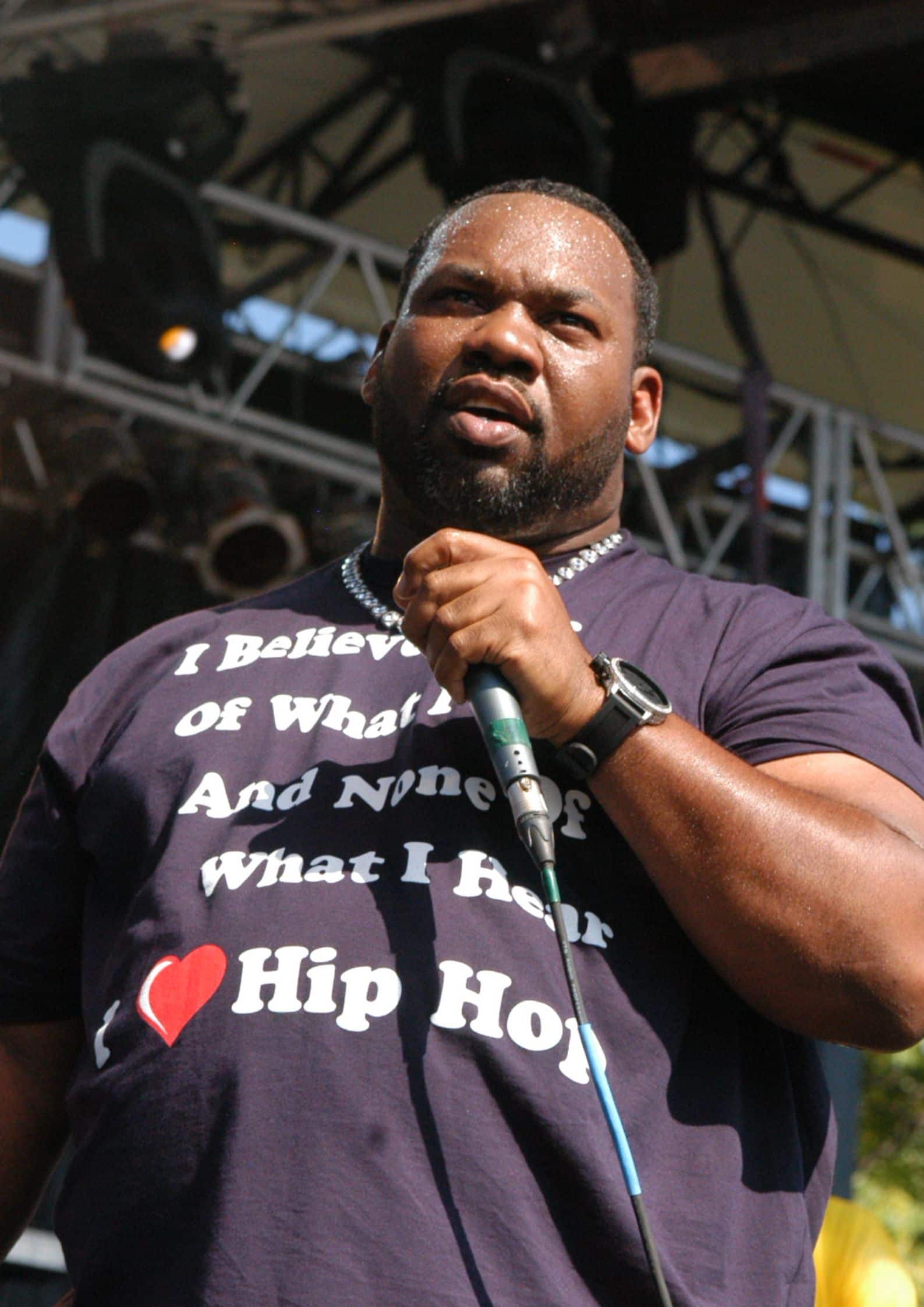 Raekwon (Corey Woods) from Wu-Tang Clan wearing a dark t-shirt with I love Hip Hop text, holding a microphone on stage.