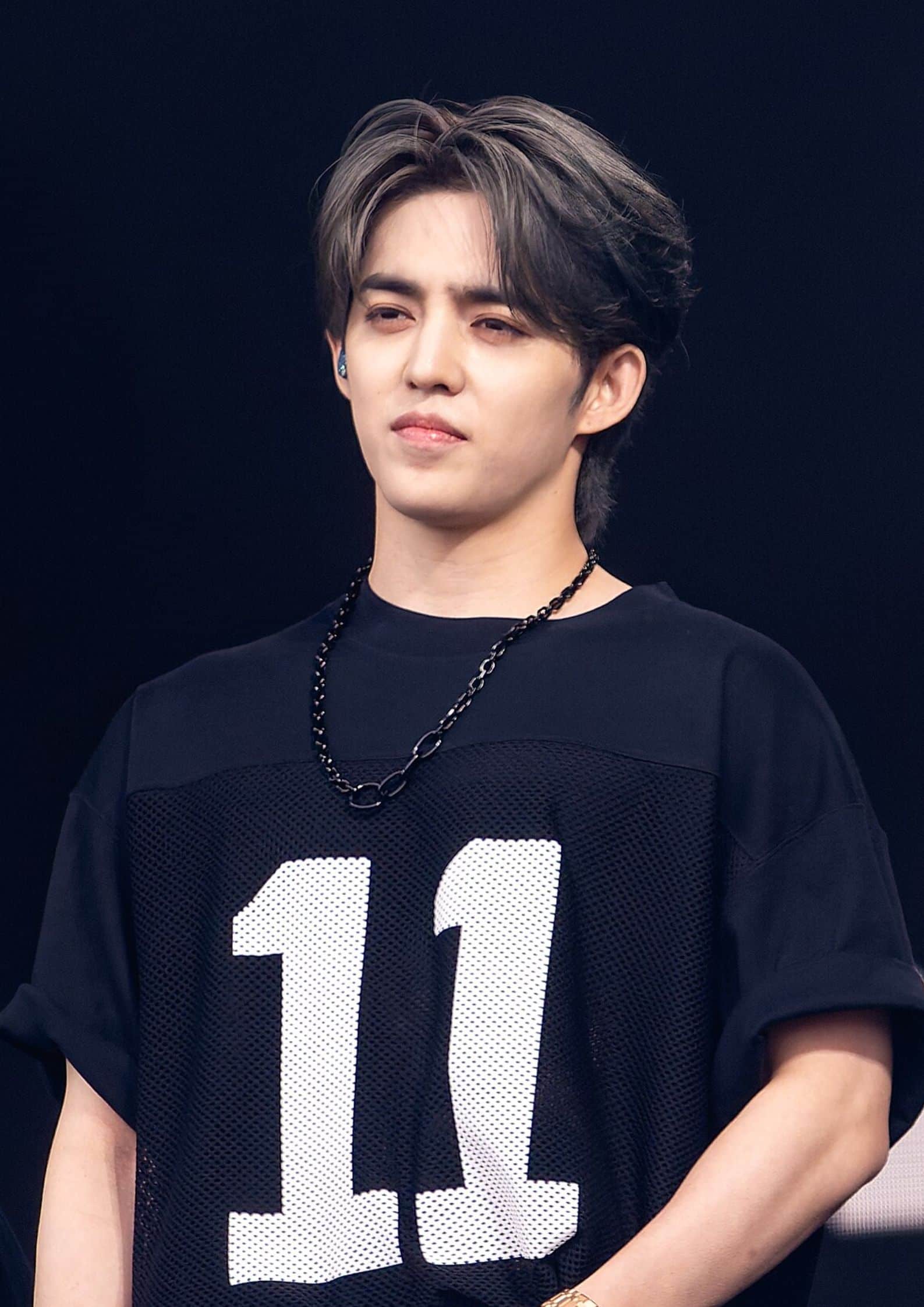 S.Coups from Seventeen wearing black jersey #11 and gold watch, standing on stage, focused and composed