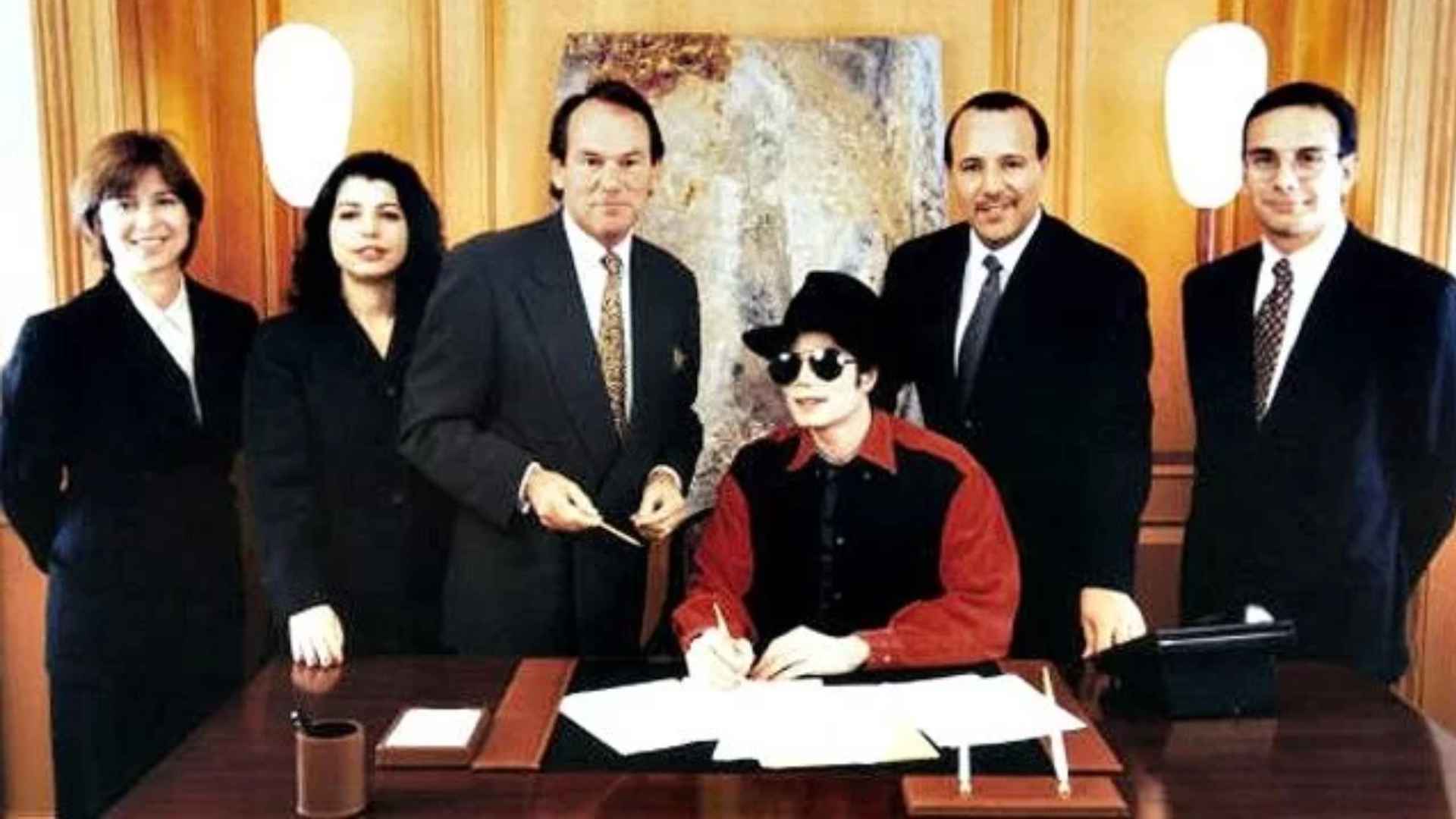 Michael Jackson signing the Sony/ATV contract surrounded by executives in a formal office setting.