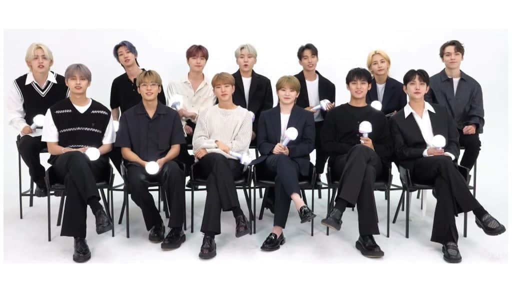 South Korean boy band Seventeen posing for a group photo holding light sticks in white studio setting