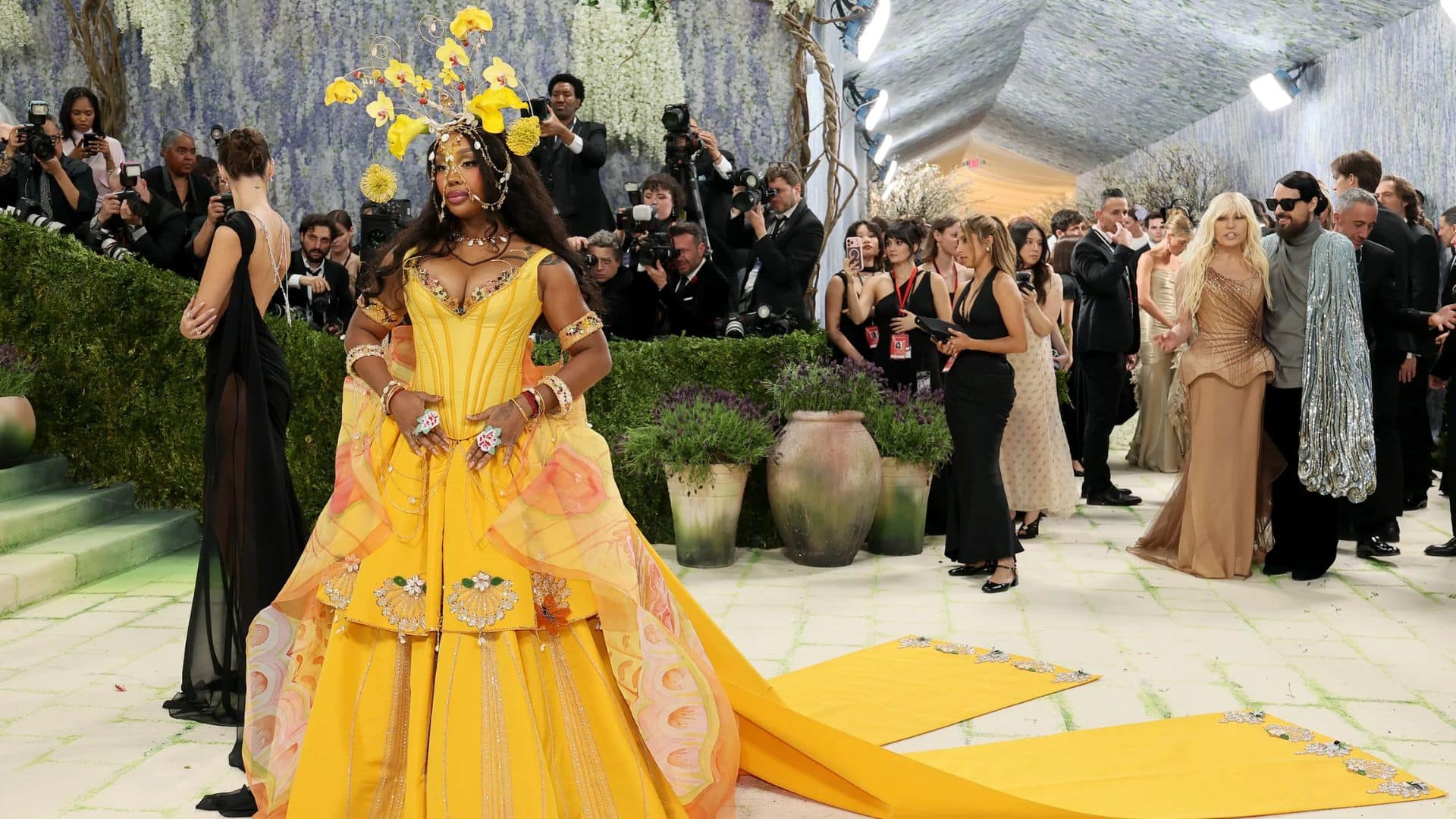 SZA wearing a vibrant yellow Bode gown with floral headpiece and dramatic train at the Met Gala 2026