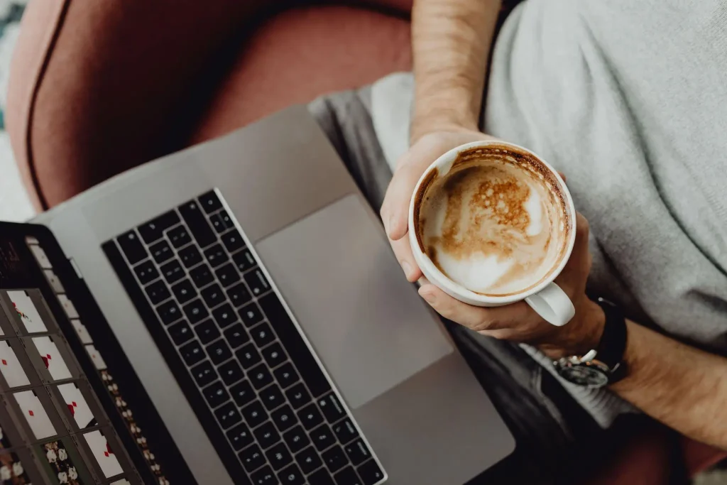Person holding a mug of coffee while using a laptop on a couch