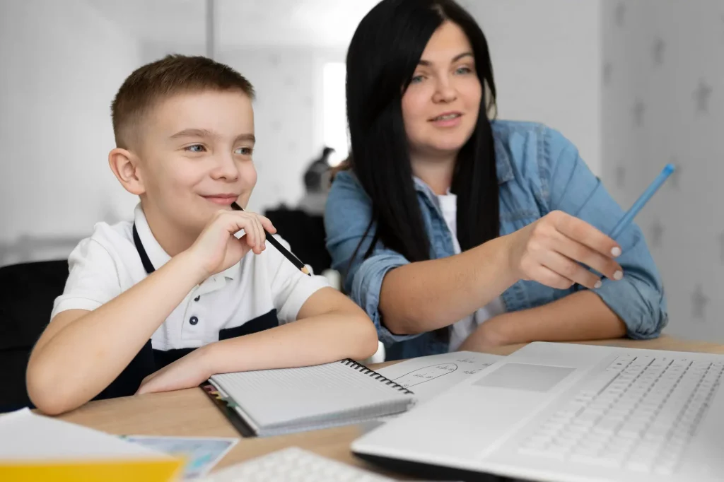 Boy and woman studying together at a desk with laptop and notebooks