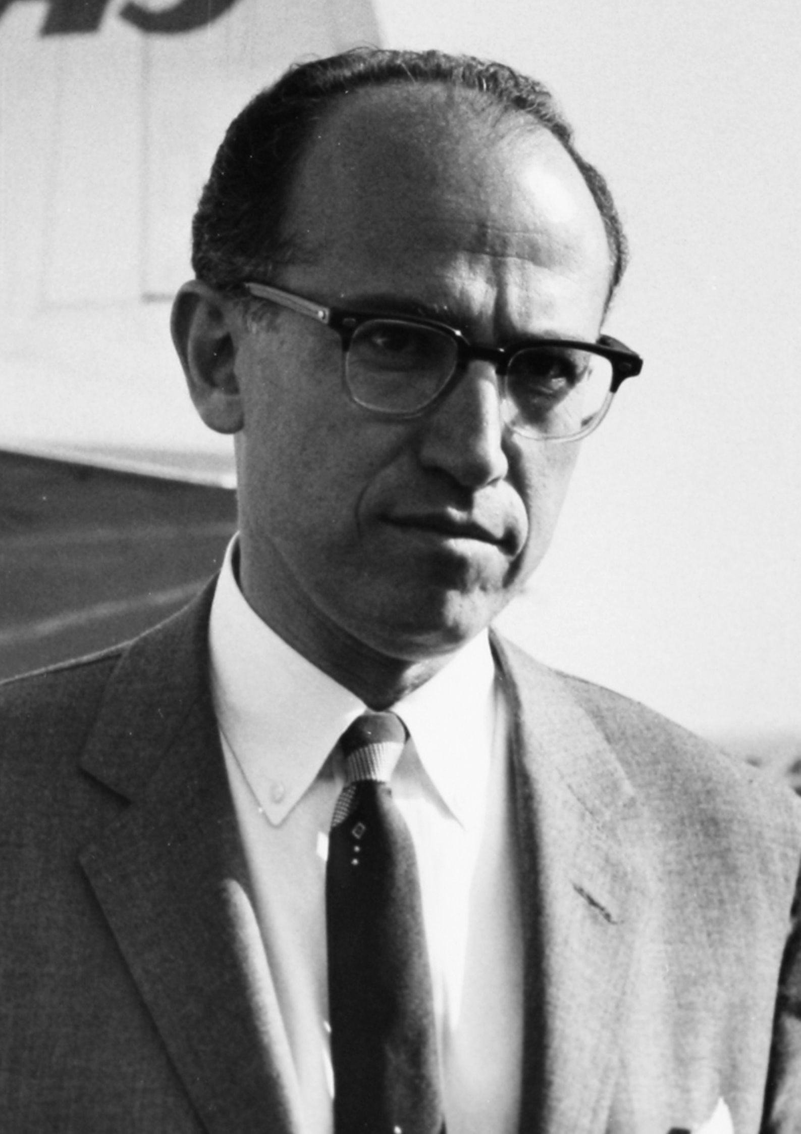 Vintage portrait of Jonas Salk wearing glasses, a suit, and patterned tie while facing the camera. (1)