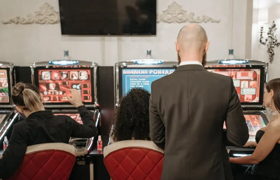 People playing slot machines in a casino with red cushioned chairs