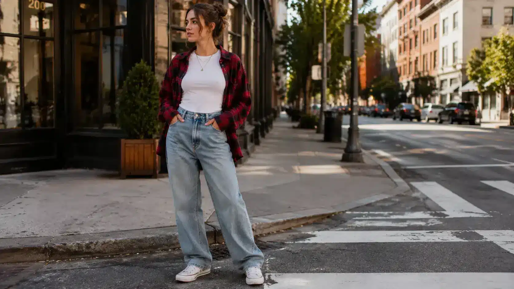 Woman wearing baggy jeans, a white t-shirt, a red flannel shirt, and white sneakers standing on a city street