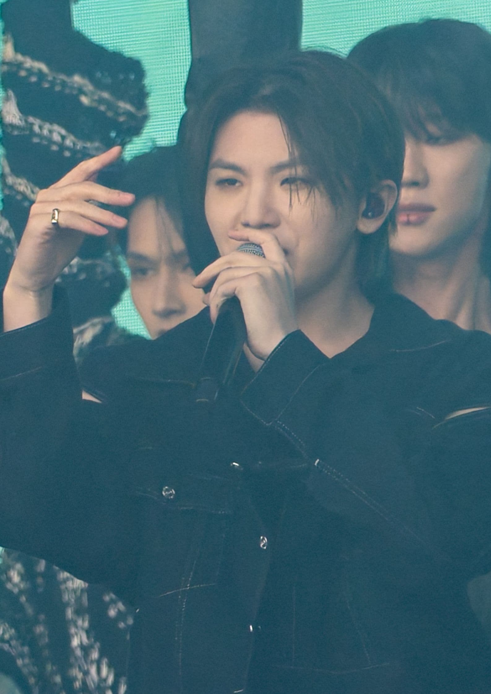 Woozi of Seventeen performs on stage, holding a mic, wearing a black denim jacket, focused on singing.