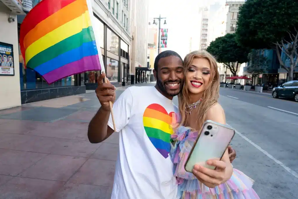 Couple taking selfie with rainbow flag on city street wearing colorful clothing