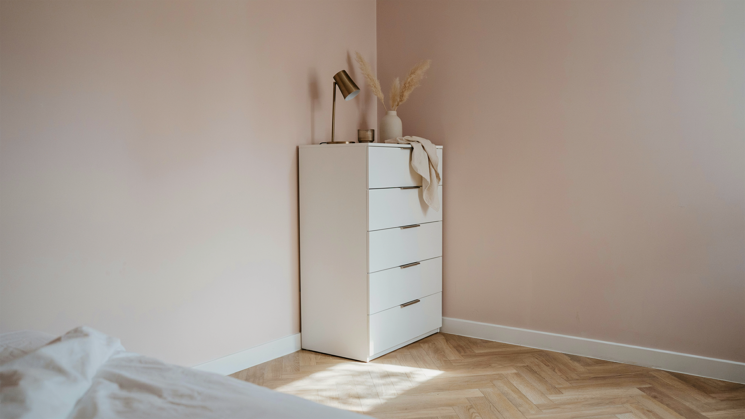 Tall, narrow dresser placed in a small bedroom corner, maximizing storage while leaving floor space open, minimalist interior.