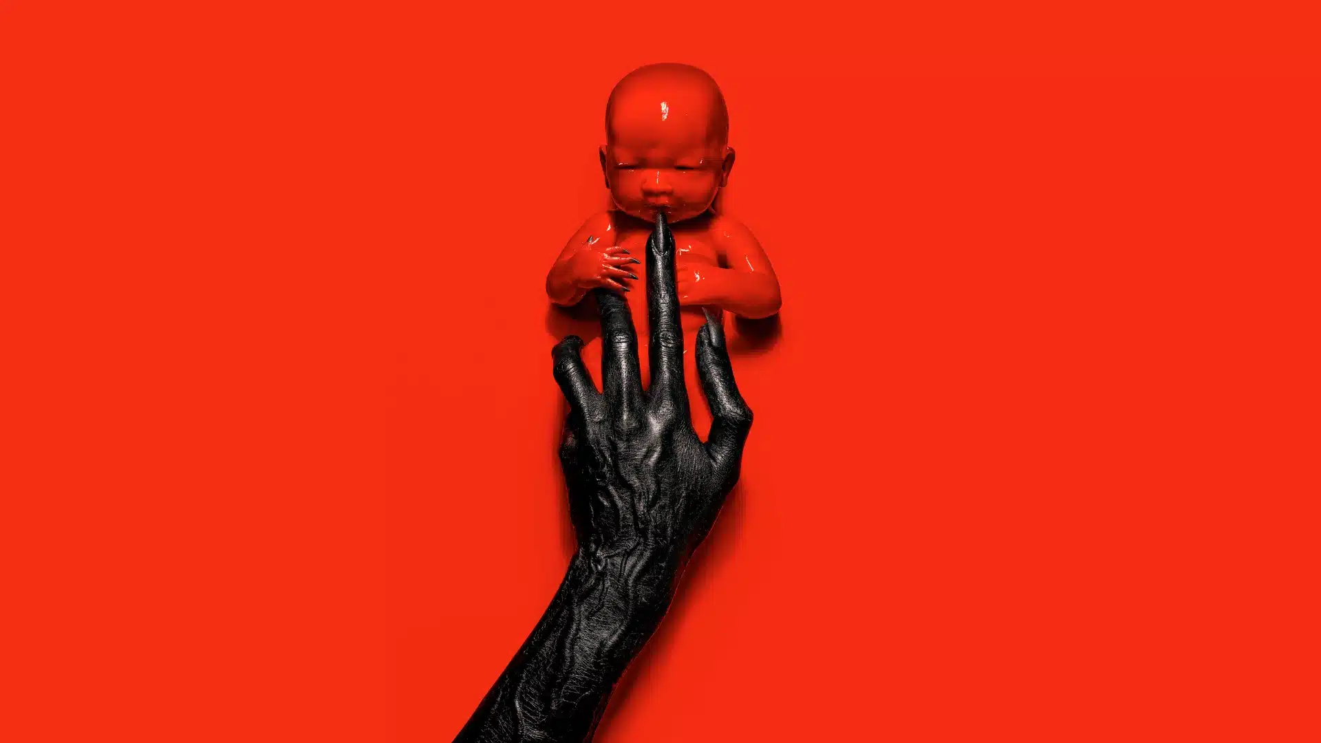 Red-toned American Horror Story Apocalypse poster showing a demonic-looking red infant being held up by a dark hand against a solid red background.