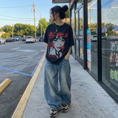 Young woman wearing baggy jeans and a black graphic tee standing outside a store.