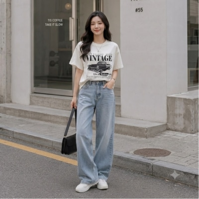 Woman wearing a vintage graphic T-shirt and wide-leg jeans, holding a black handbag, standing on a city sidewalk.