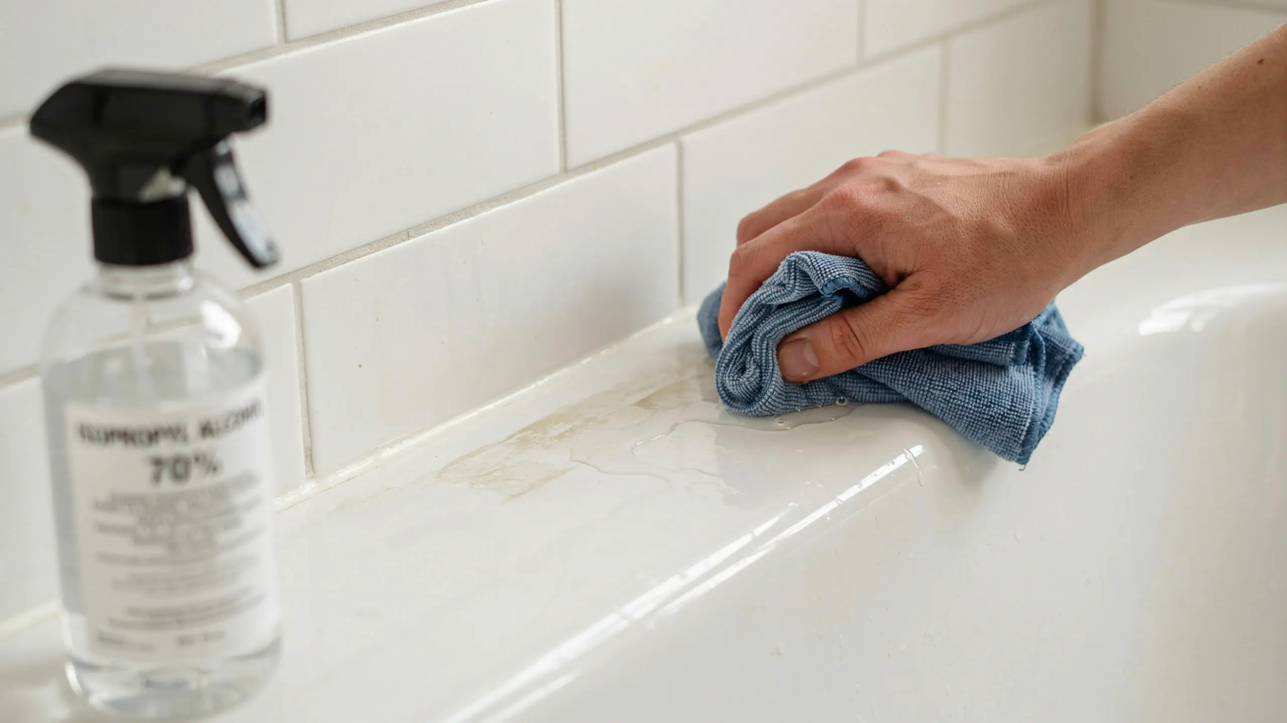 Wiping bathtub seam with cloth and rubbing alcohol to clean before caulking.
