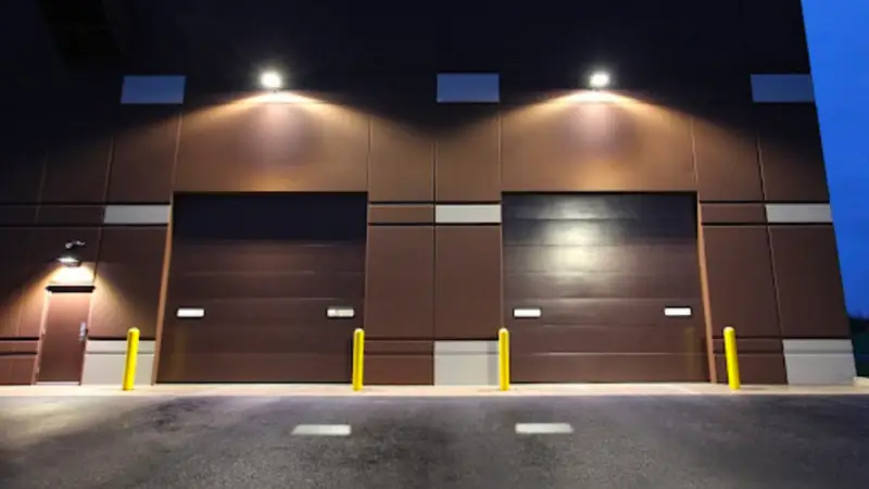 Two large closed garage doors with overhead lighting on industrial building exterior