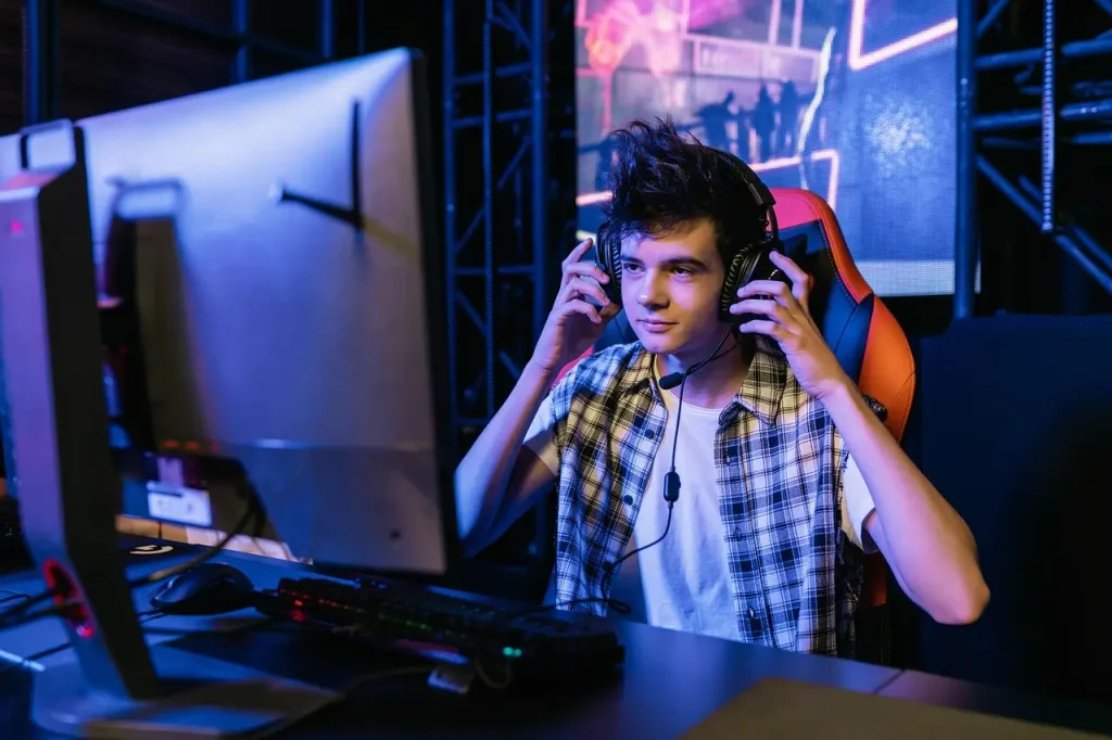 Teen playing video game at computer desk with headset in dimly lit gaming setup