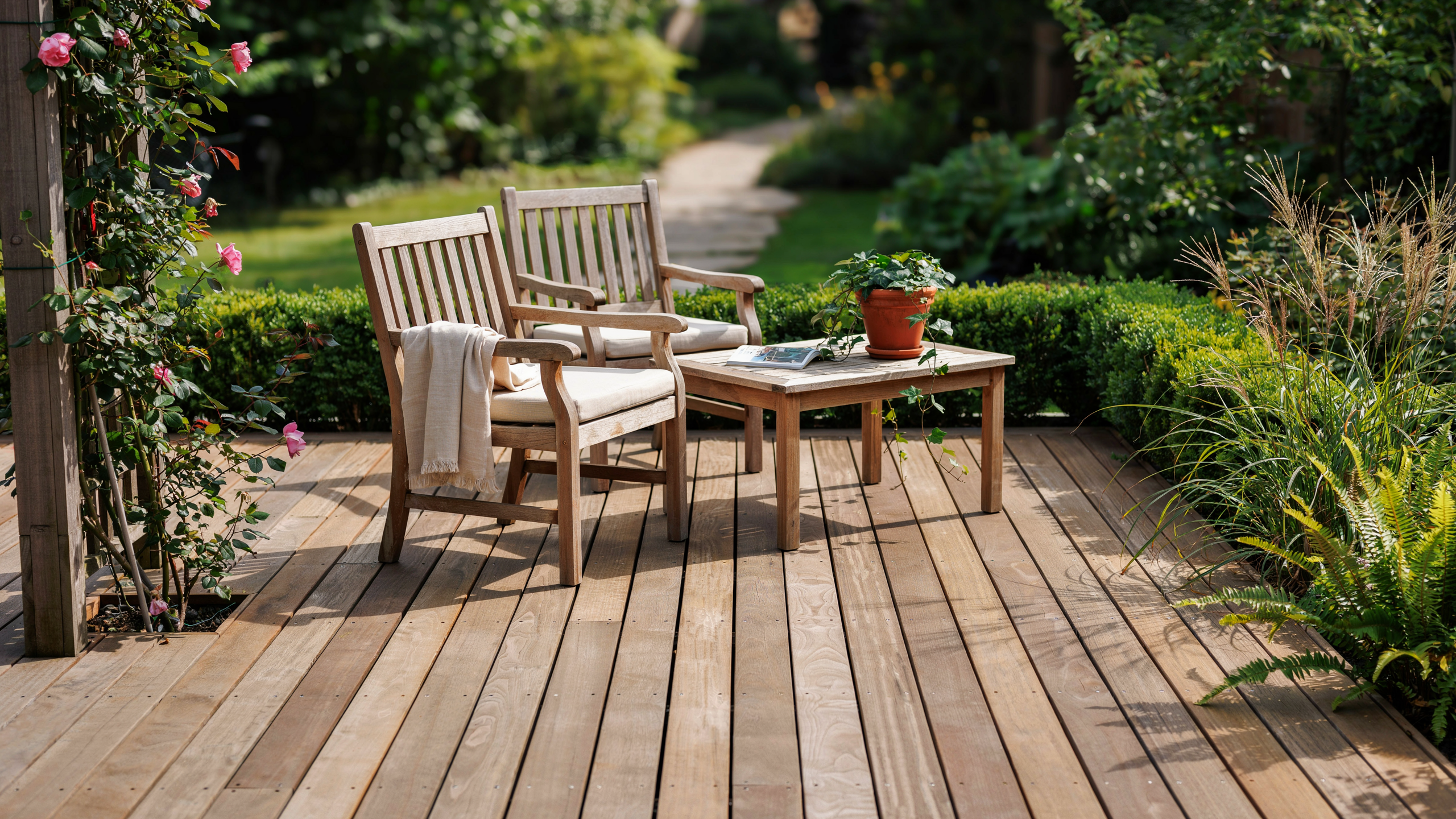 Wooden outdoor patio furniture set on a deck surrounded by greenery in natural sunlight, no people or text.