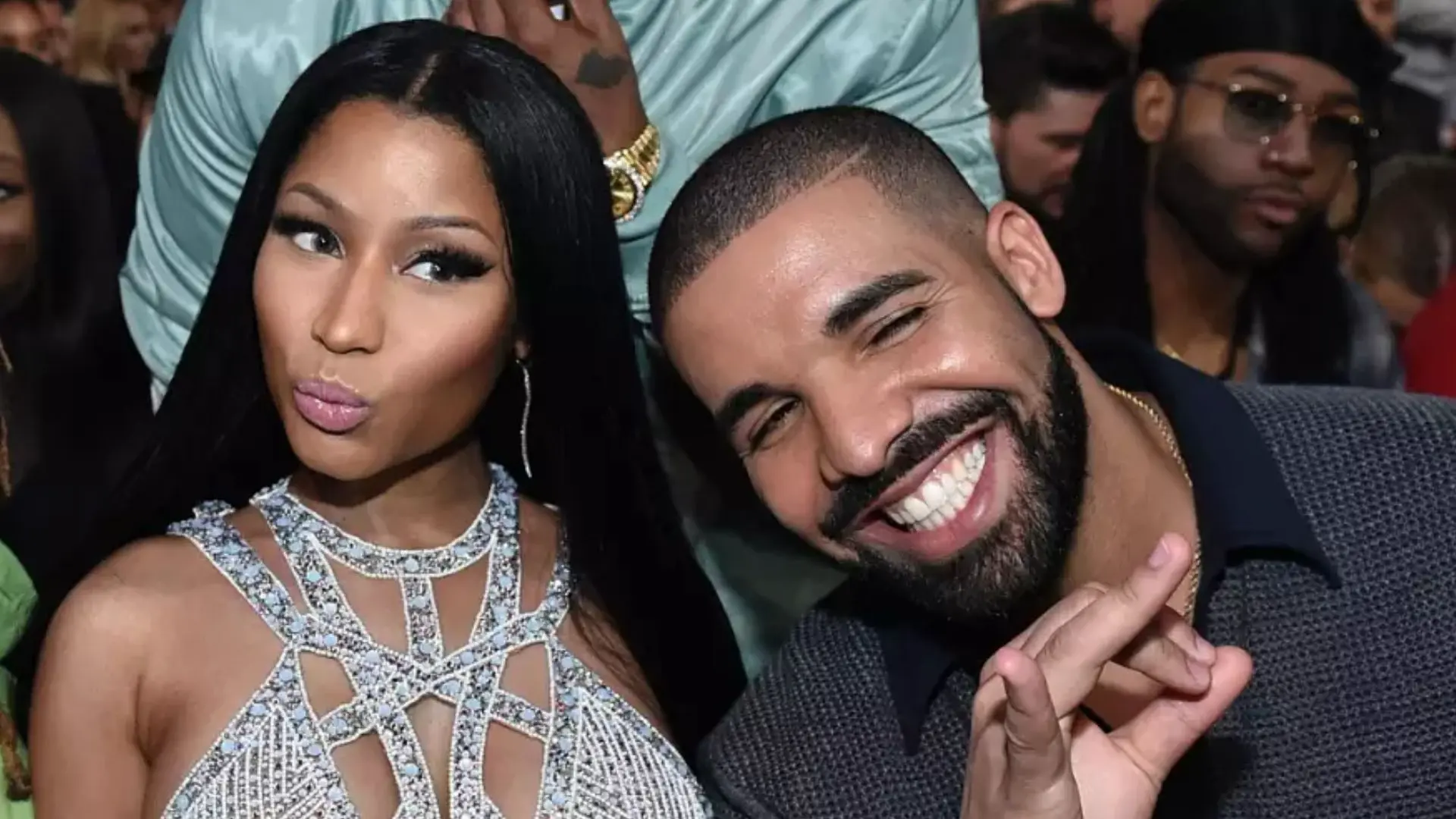 Nicki Minaj and Drake smiling and posing together at a crowded awards event, with Nicki wearing a sparkling embellished dress