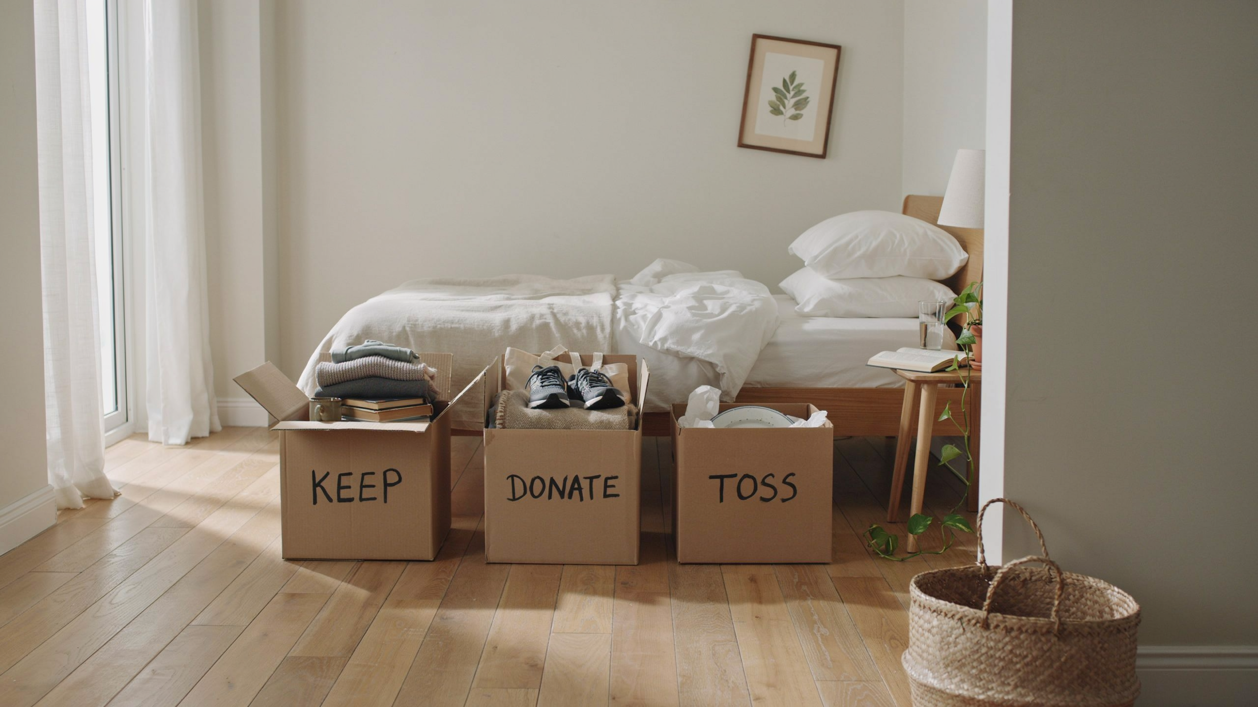 Bedroom with items sorted into keep, donate, and toss bins, minimal clutter.