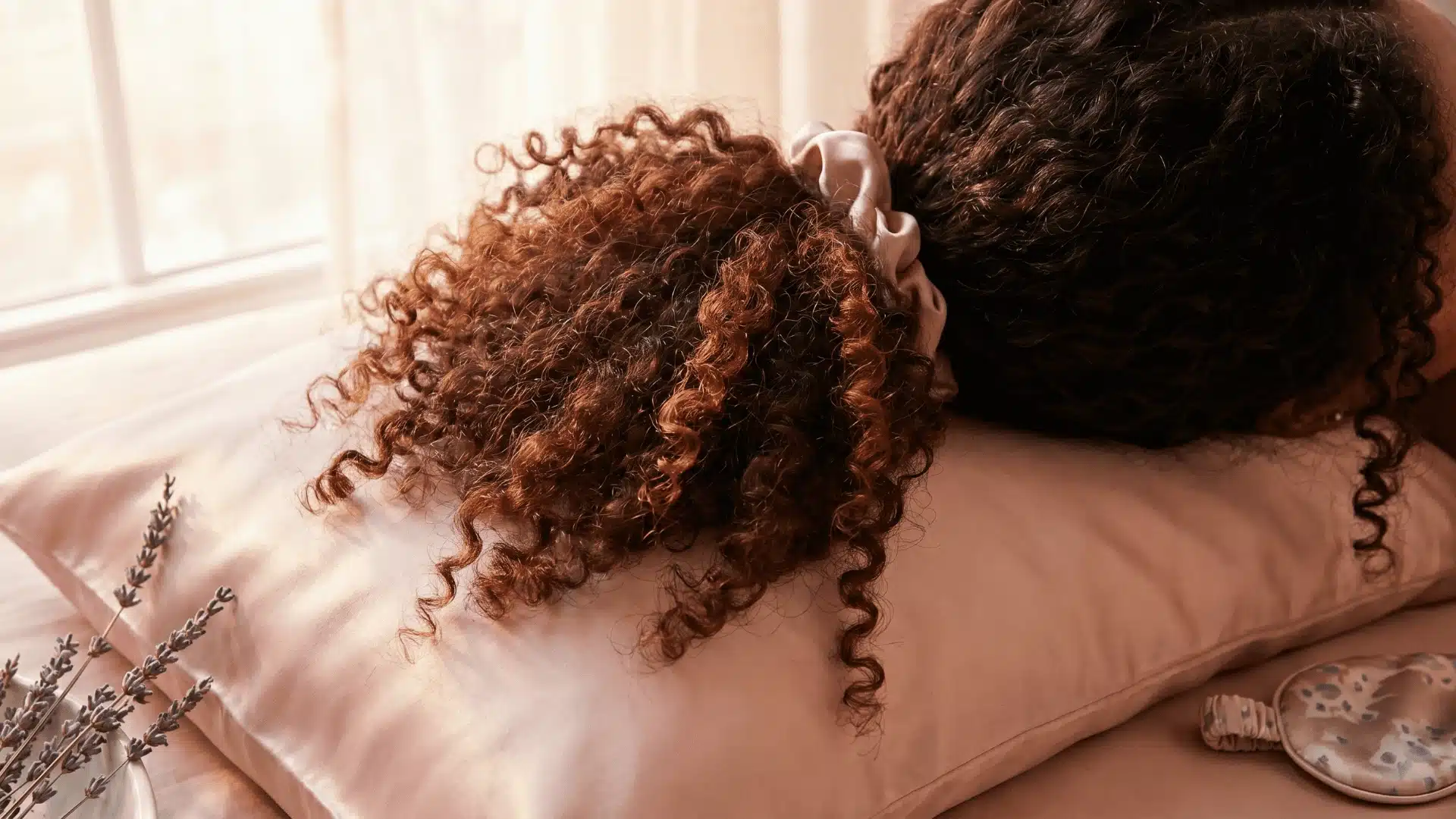 Curly hair gathered in a pineapple on a satin pillowcase to maintain curl shape and reduce friction overnight.
