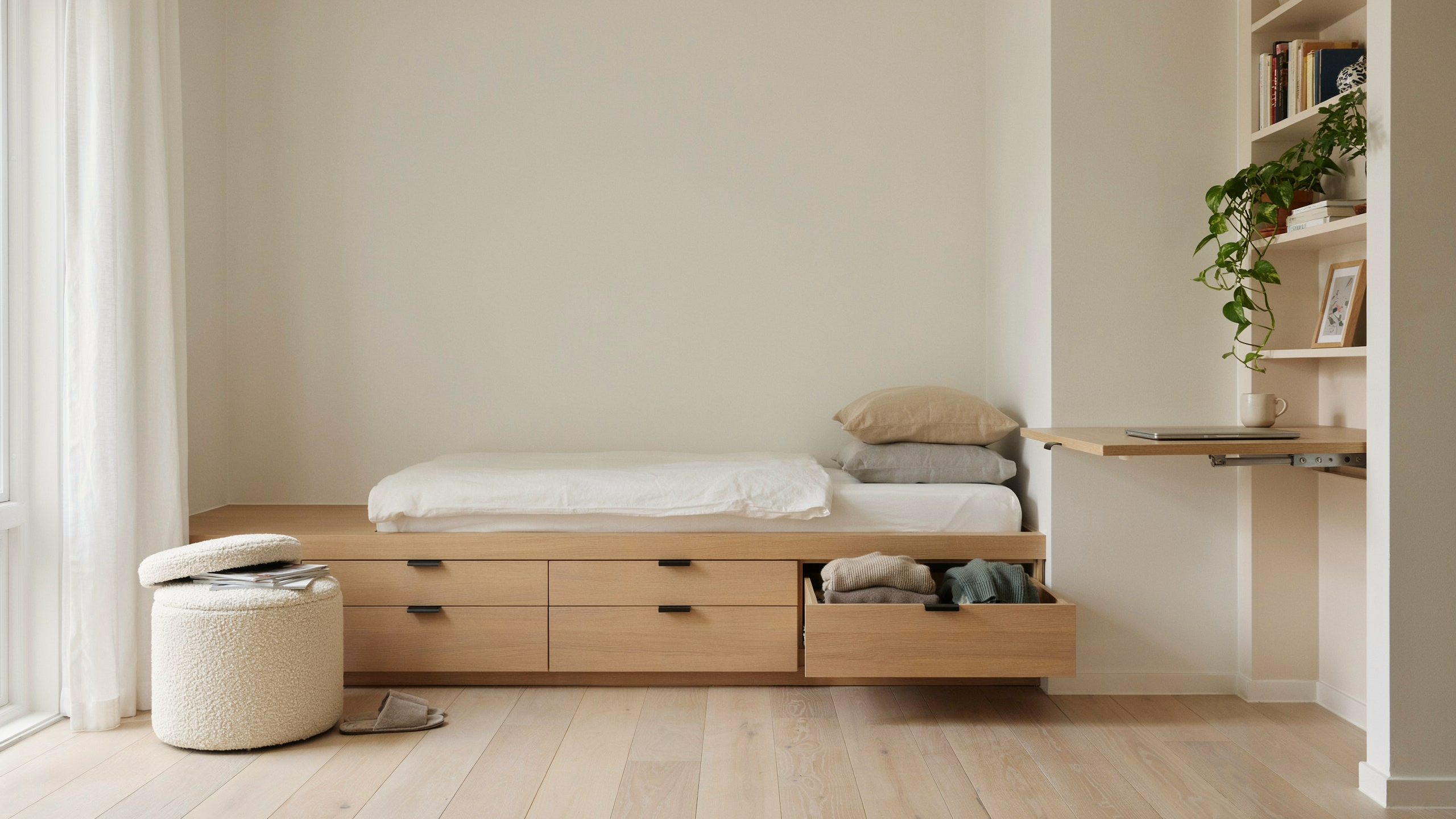 Room with bed drawers, storage ottoman, and fold-away desk, minimalist setup.