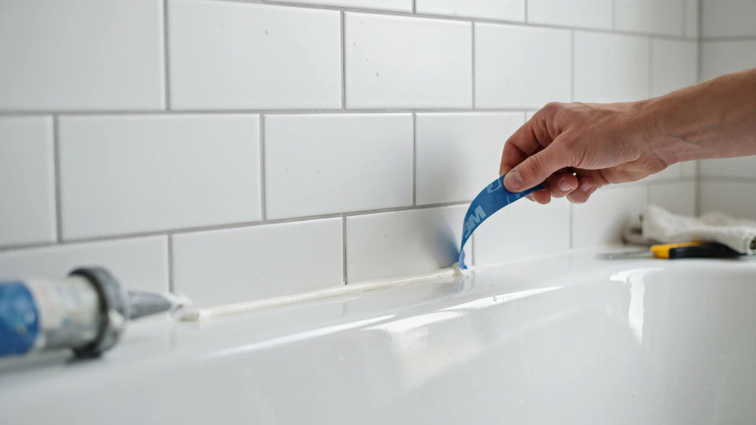 Pulling painter’s tape from caulk line, revealing neat straight finish.
