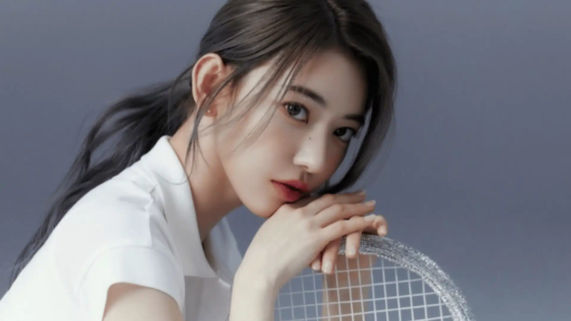 Female K-pop idol in close-up portrait, leaning on a round metallic mesh surface, soft grey background, calm expression with natural makeup and tied-back dark hair.