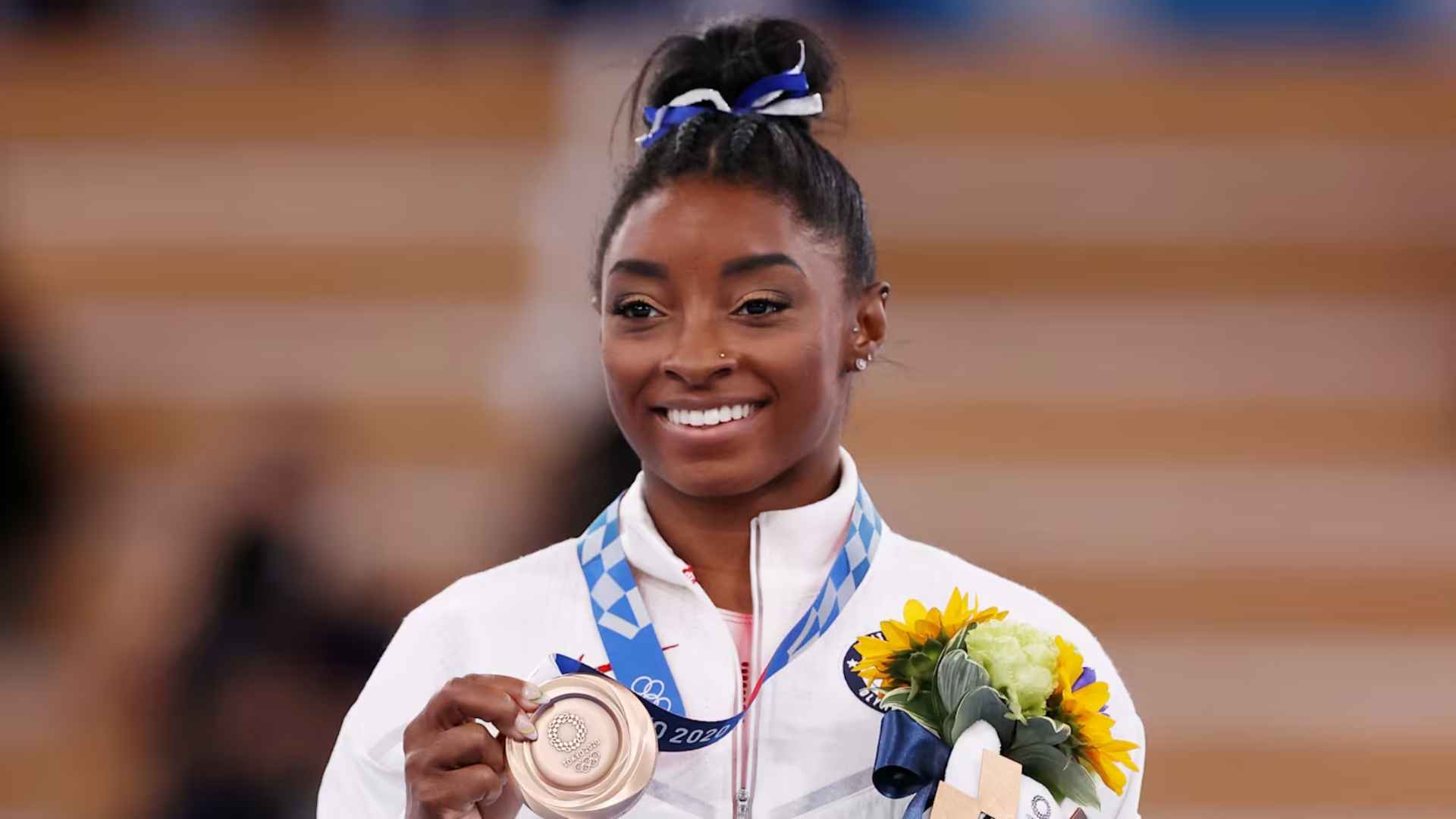Simone Biles smiling with Olympic medal and flowers