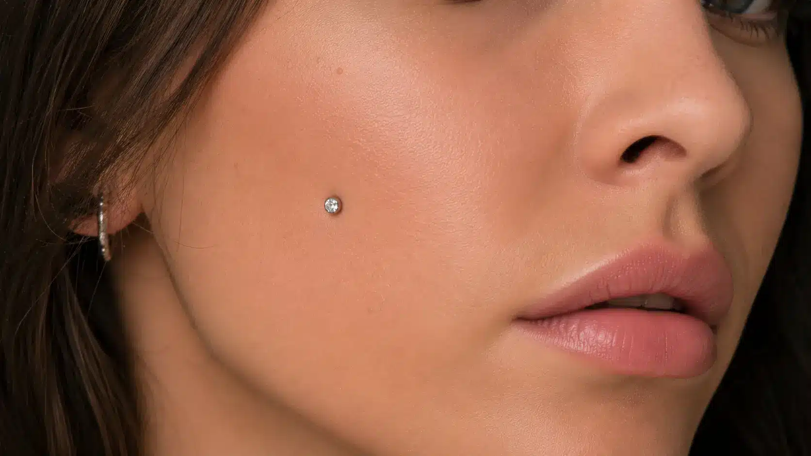Single cheek dermal piercing with a gemstone top