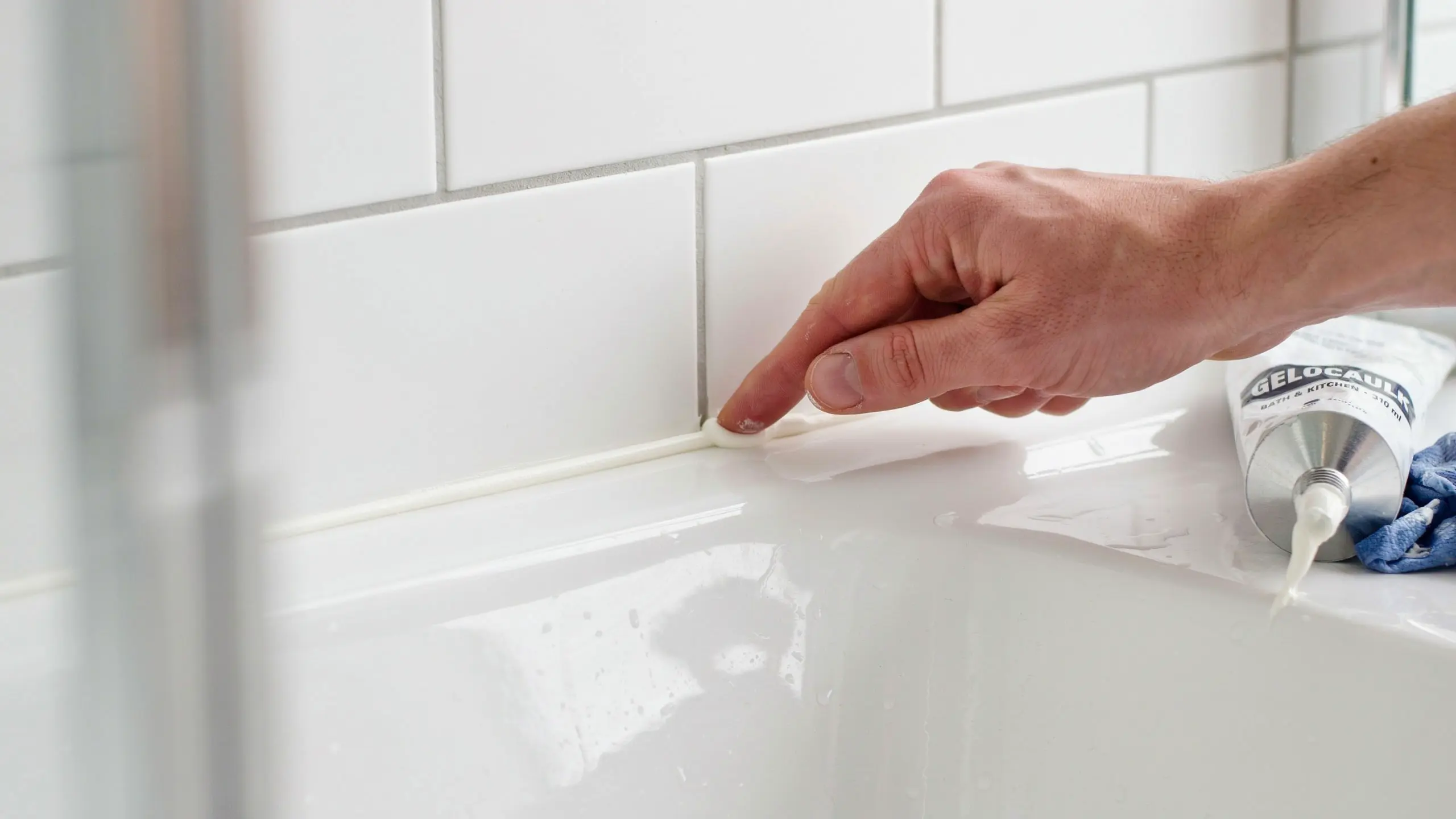 Finger smoothing freshly applied caulk line along bathtub edge for even finish.