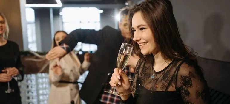 Woman holding champagne glass smiling at social gathering in warmly lit indoor setting