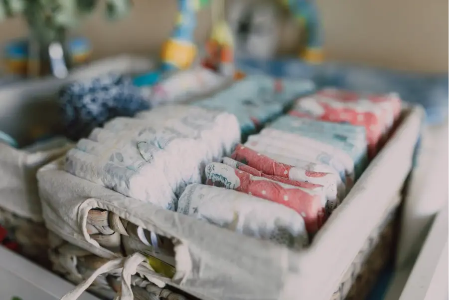Colorful baby diapers neatly arranged in woven basket on nursery changing table