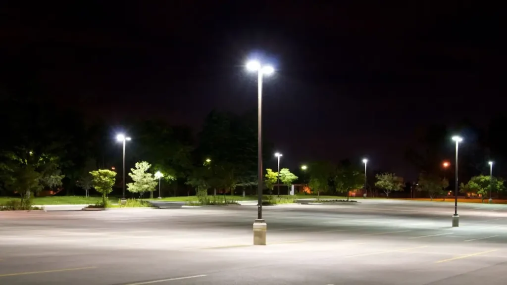 Empty parking lot illuminated by streetlights at night with trees in the background