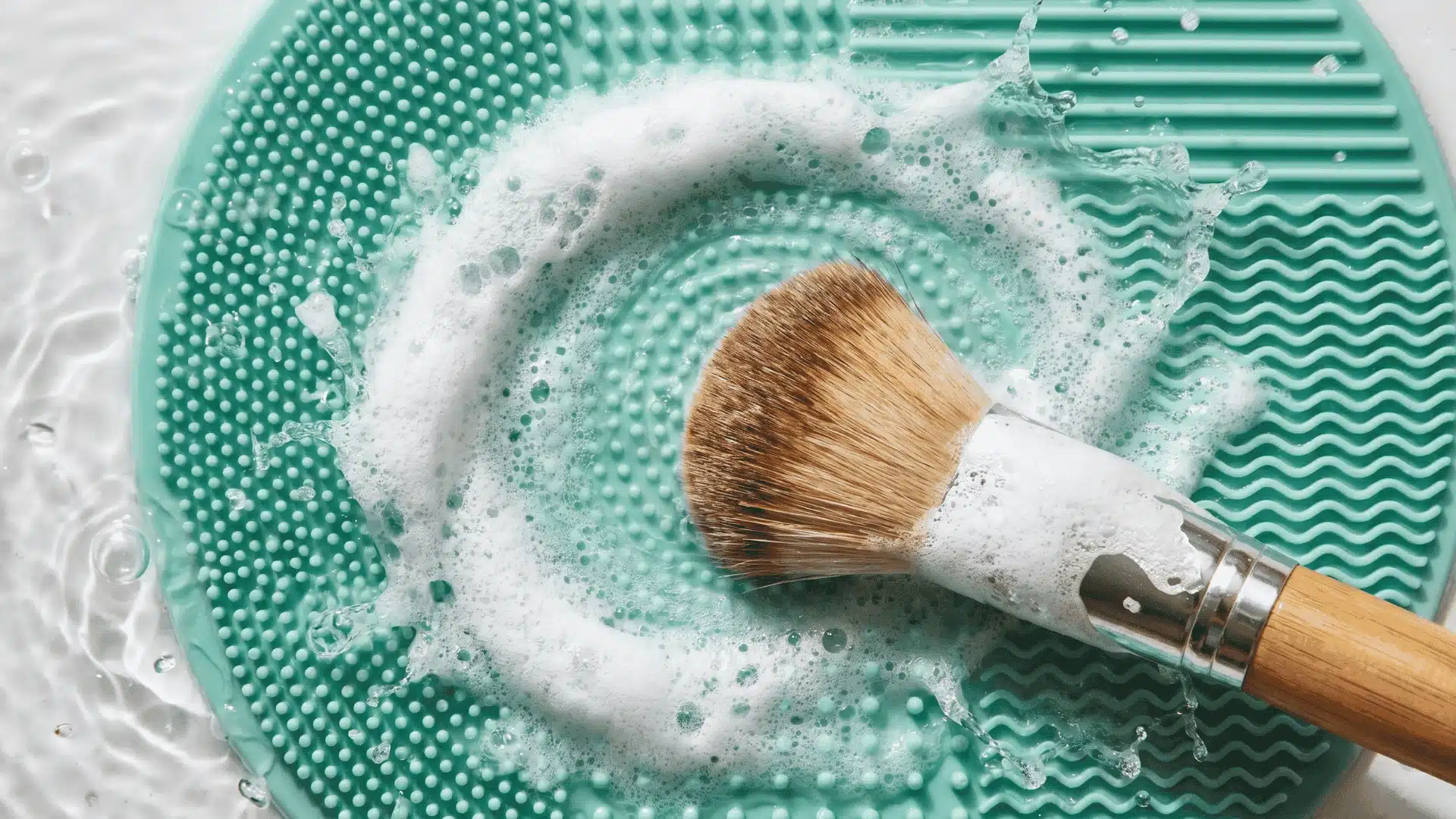 A makeup brush being swirled on a silicone mat with foam forming to show lathering and cleaning technique.