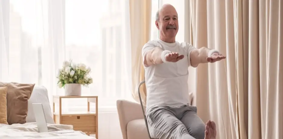 Man stretching on chair in sunlit bedroom, beige curtains and cozy bedding nearby
