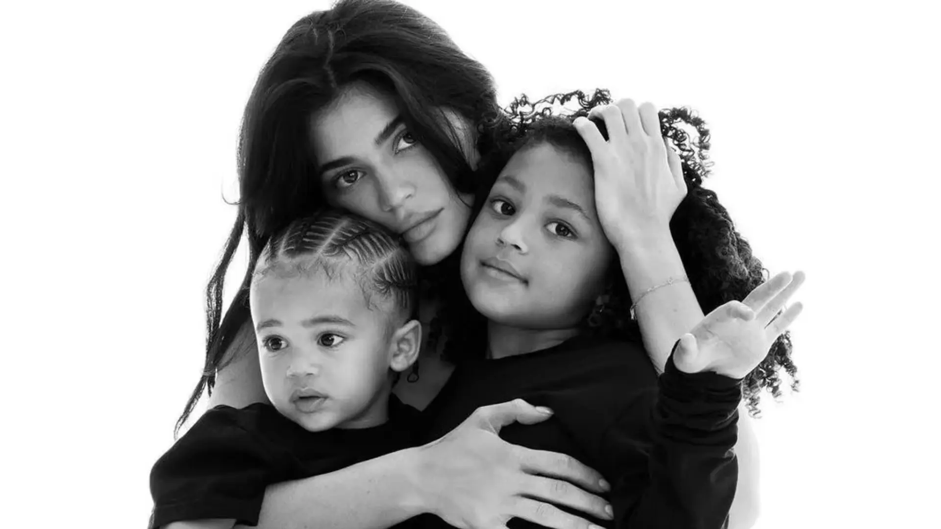 Black and white portrait showing an adult embracing two children with a warm family moment and gentle expressions