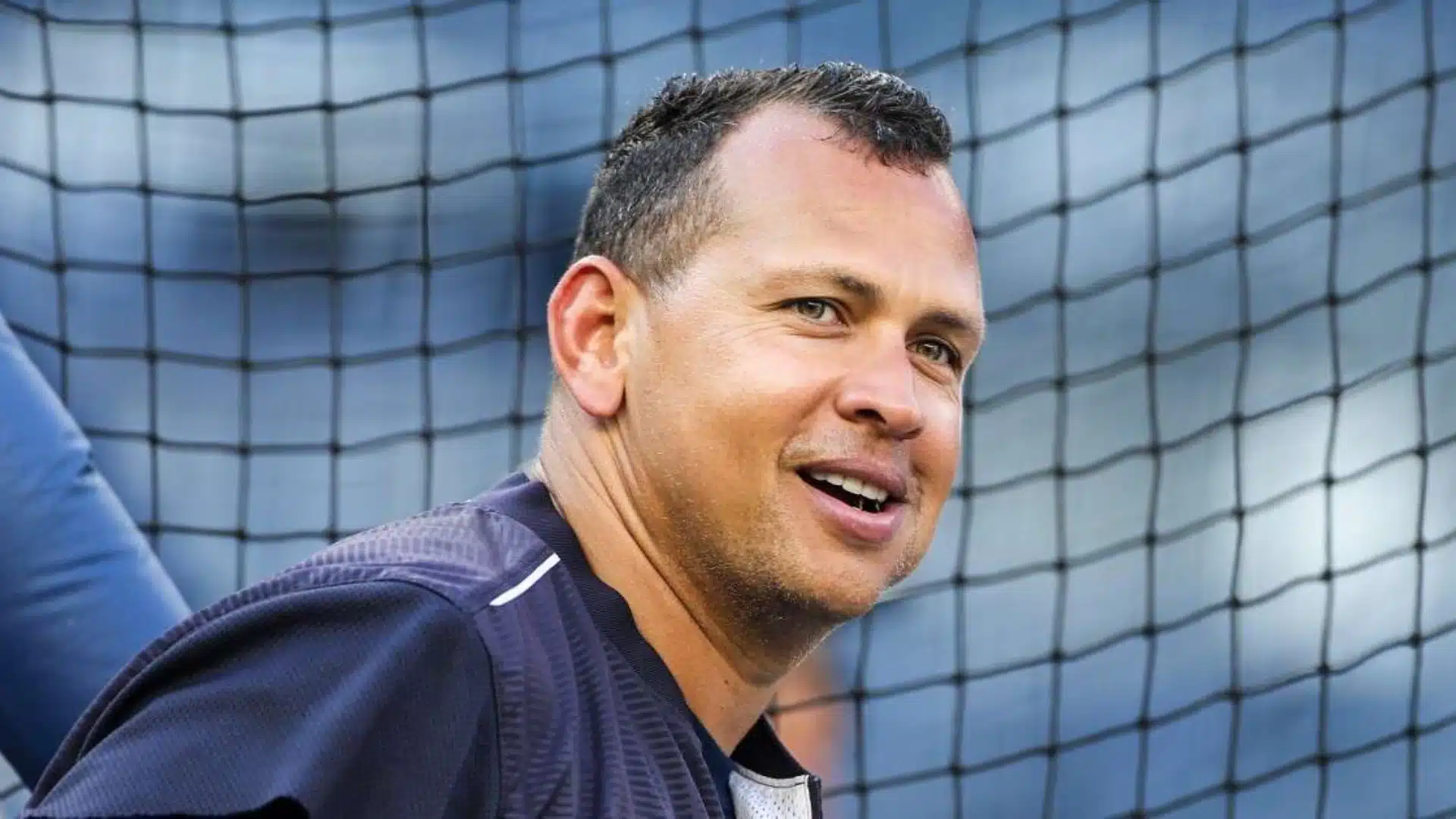 Baseball player smiling near a protective net at a stadium during practice.