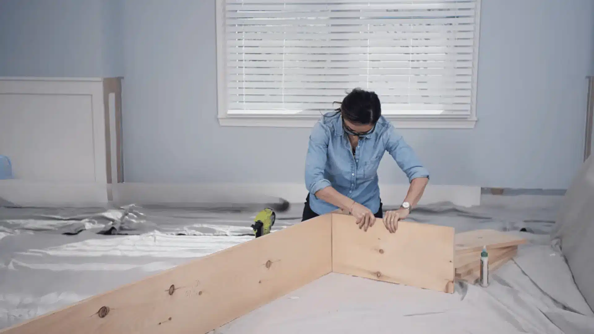 Person assembling wooden shelf pieces on a covered floor during a DIY shelving project