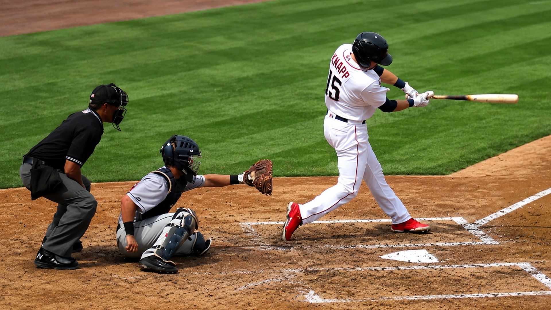 Baseball batter swinging at pitch with catcher and umpire behind home plate on infield dirt