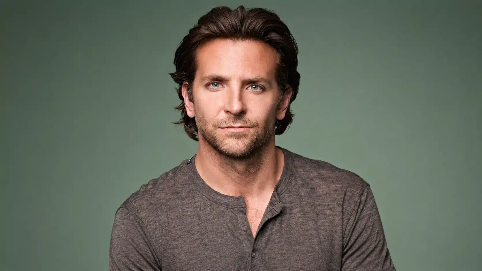 Portrait of bradley cooper with swept-back brown hair and textured shirt against a muted green studio backdrop