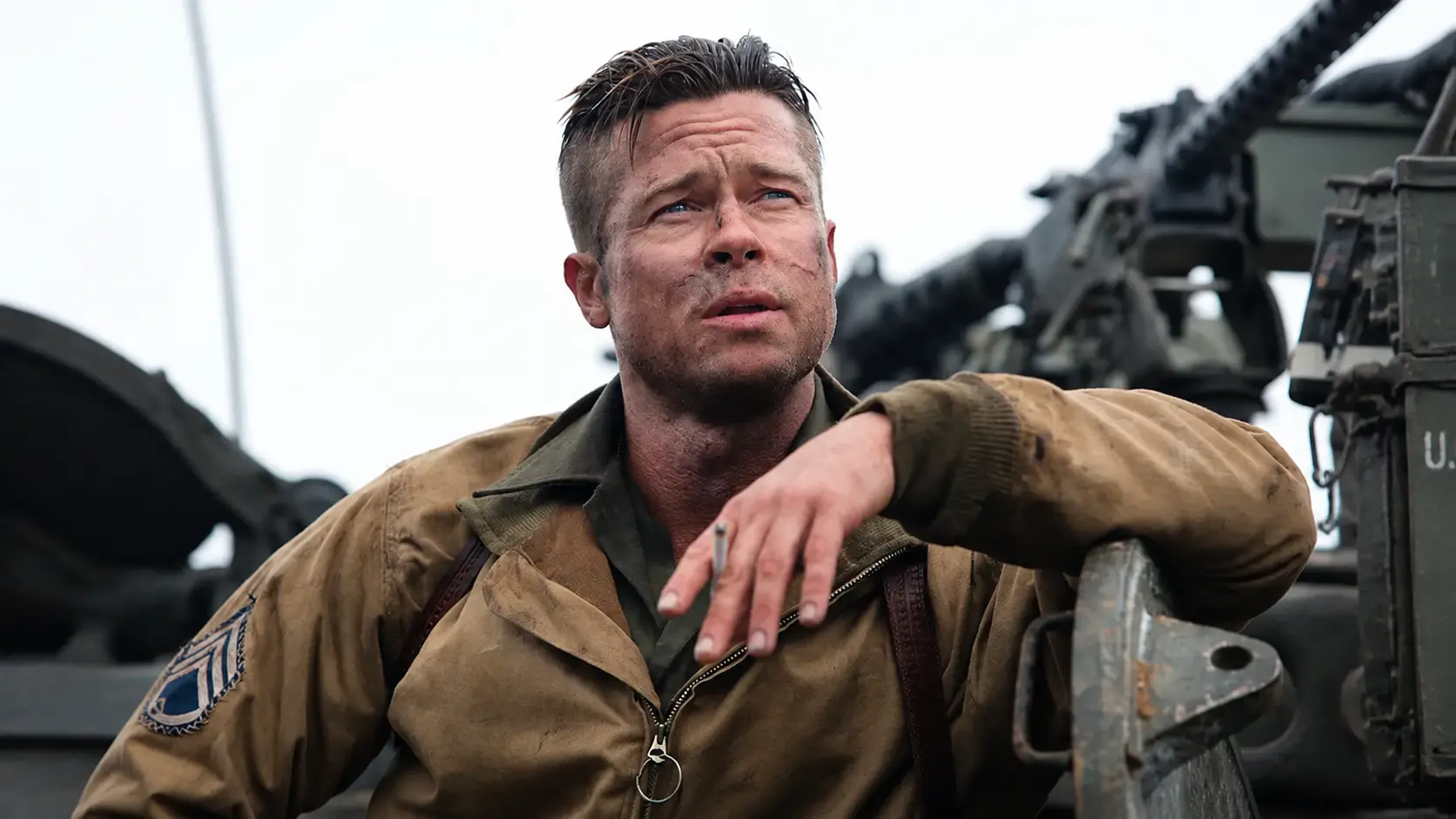 Brad pitt leaning on military vehicle under grey sky with cigarette in hand and dirt-streaked face portrait