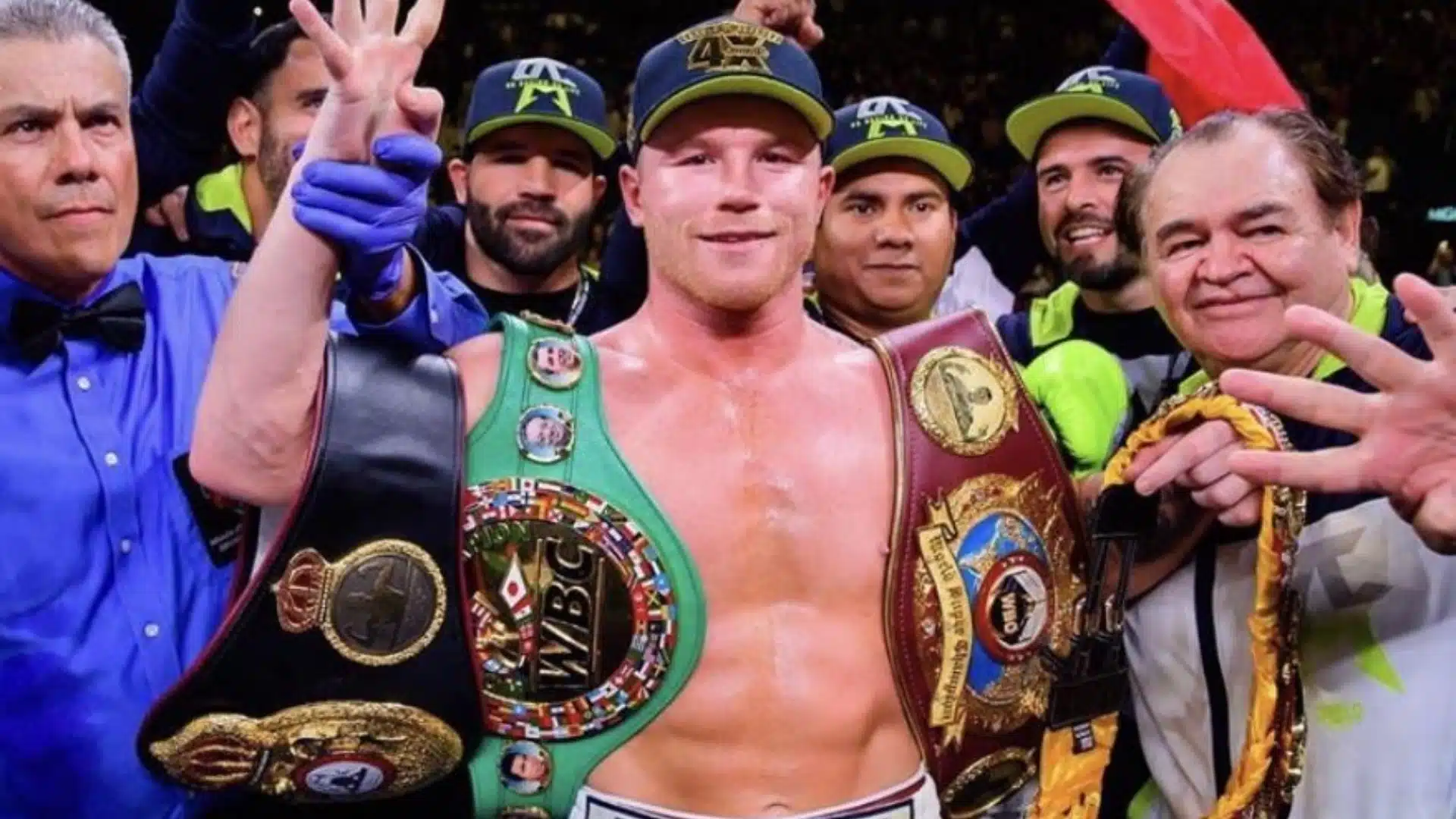 Boxer celebrating with championship belts surrounded by team members after a fight victory.
