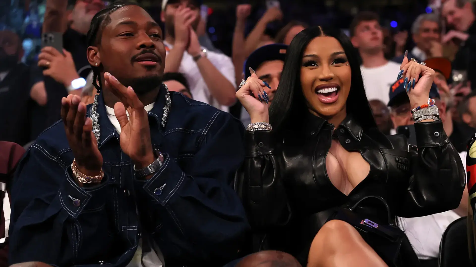 Cardi B and Stefon Diggs cheering courtside together at a basketball game, both dressed in black.