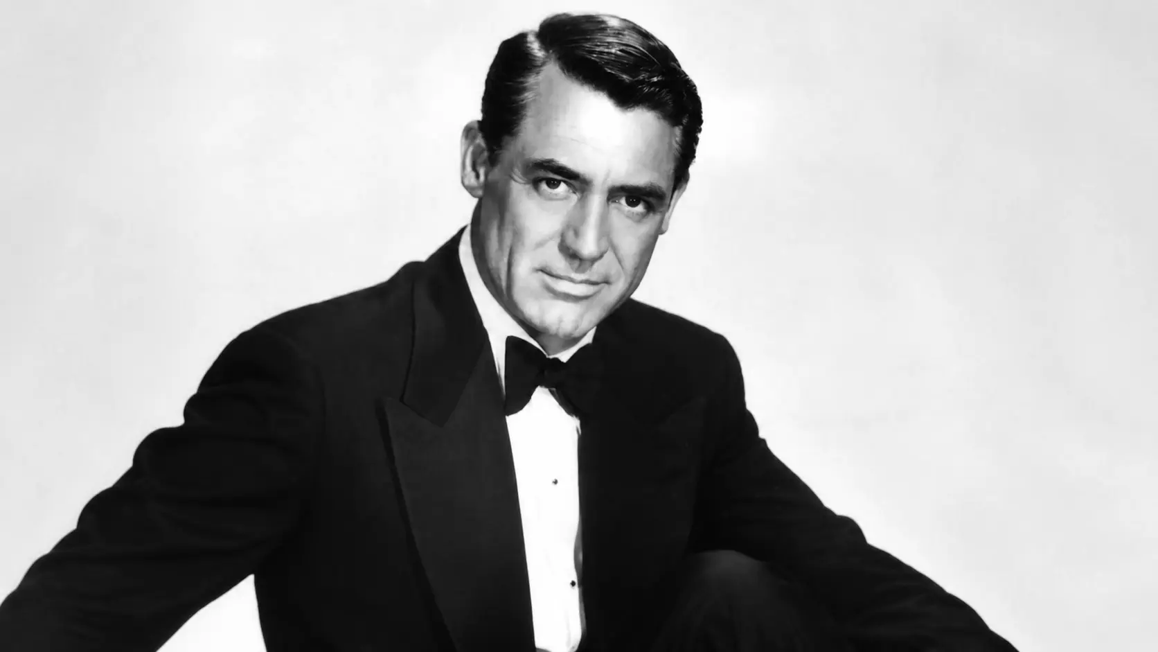 black and white tuxedo portrait showing cary grant seated with a confident pose and a formal studio backdrop