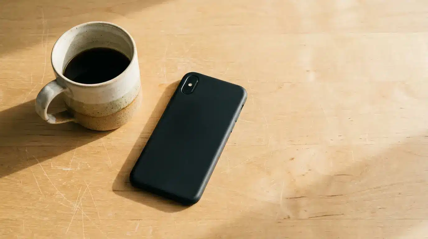 Ceramic coffee mug and smartphone on wooden table in natural sunlight